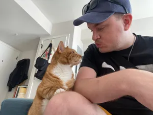 Edward leaning in to kiss Hubert, an orange and white tabby cat perched against his shoulder