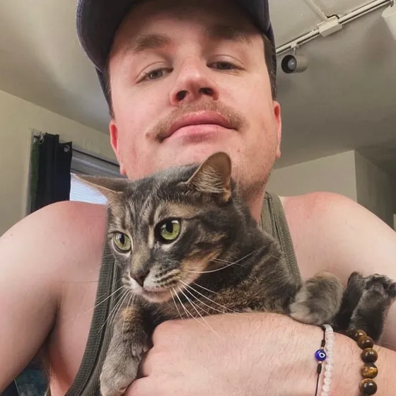 Edward holding Stellaluna, a grey tabby cat, against his chest indoors