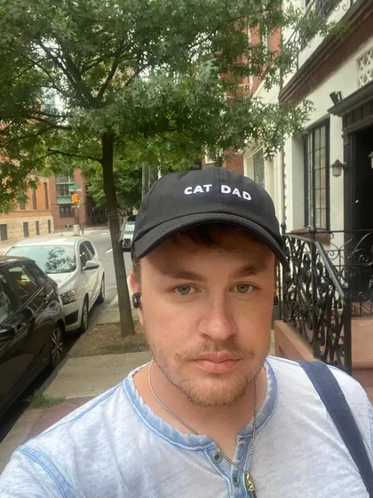 Edward wearing a black cap embroidered "CAT DAD", standing on a tree-lined Philadelphia street