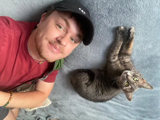 Edward lying on a blue blanket beside Stellaluna, a grey tabby cat, both looking up at the camera