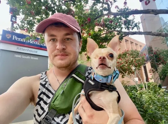Edward holding Zoe, a small cream chihuahua in a blue harness, outside Penn Medicine Rittenhouse